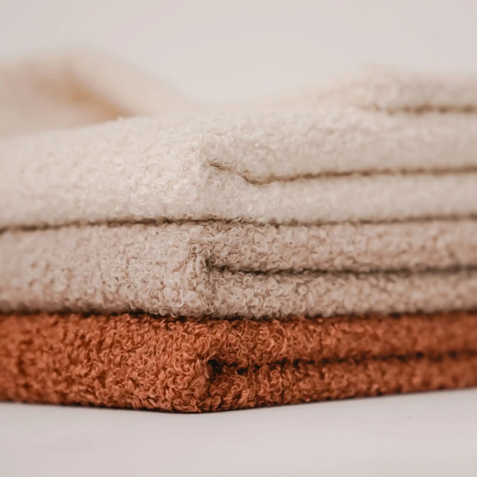 Zbliżenie na detale. 3 kocyki dla psa, w kolorze nugat (rudo-brązowy), pralinka (jasno brązowy), chałwa (kremowy), ułożone jeden na drugim od najjaśniejszego do najciemniejszego. Nowoczesna, wysokiej jakości tkanina boucle z certyfikatami bezpieczeństwa.