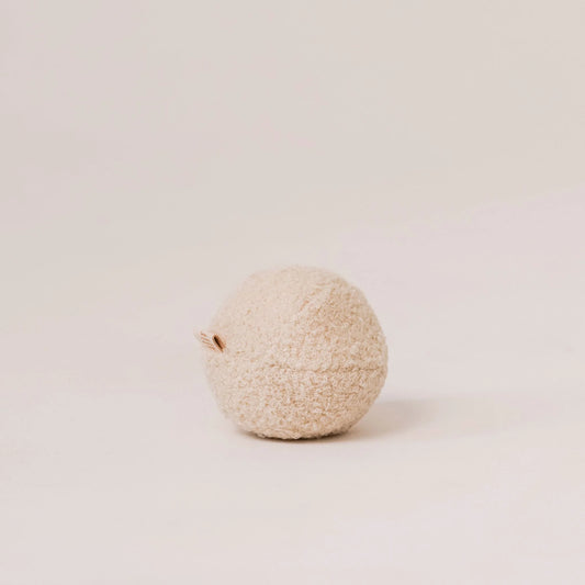 Miękka piłka dla psa z tkaniny boucle w kolorze chałwa (kremowy). Widoczna metka z logo. Jasne, czyste tło.