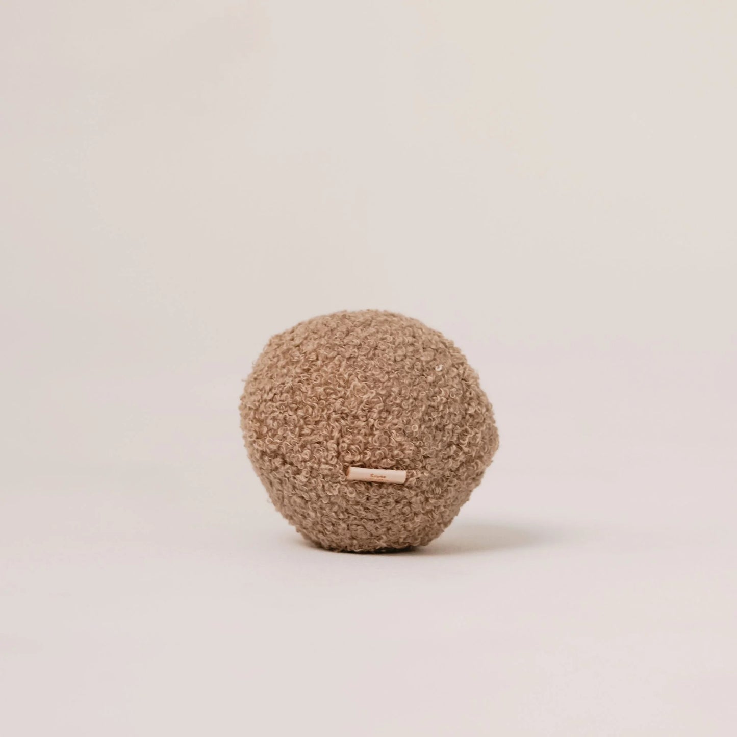 Miękka piłka dla psa z tkaniny boucle w kolorze pralinka (jasny brąz). Widoczna metka. Jasne, czyste tło.