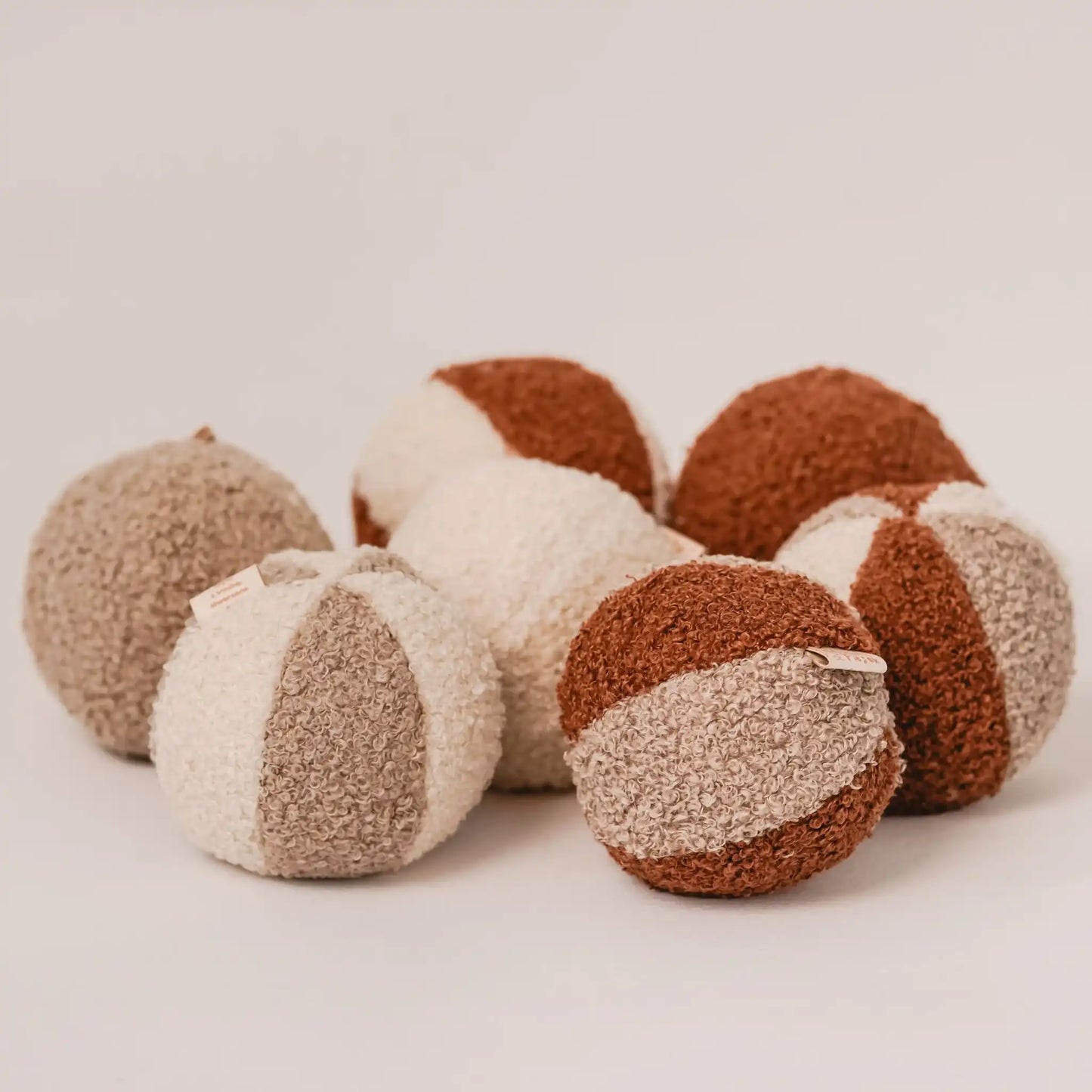 Kilka piłeczek dla psa, różnokolorowych (rudo-brązowy, jasny brąz, kremowy), zbliżenie, metki. Tkanina boucle.