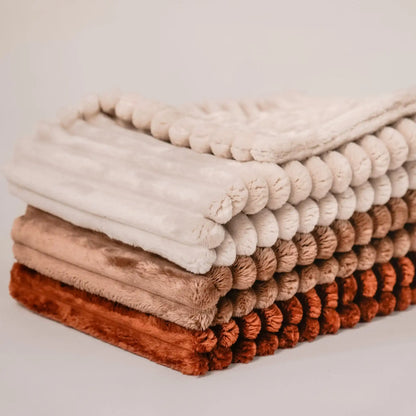 Zbliżenie na detale. 3 kocyki dla psa, w kolorze cynamonek (rudo-brązowy), ciasteczko (brązowy), beza (kremowy), ułożone jeden na drugim od najjaśniejszego do najciemniejszego.