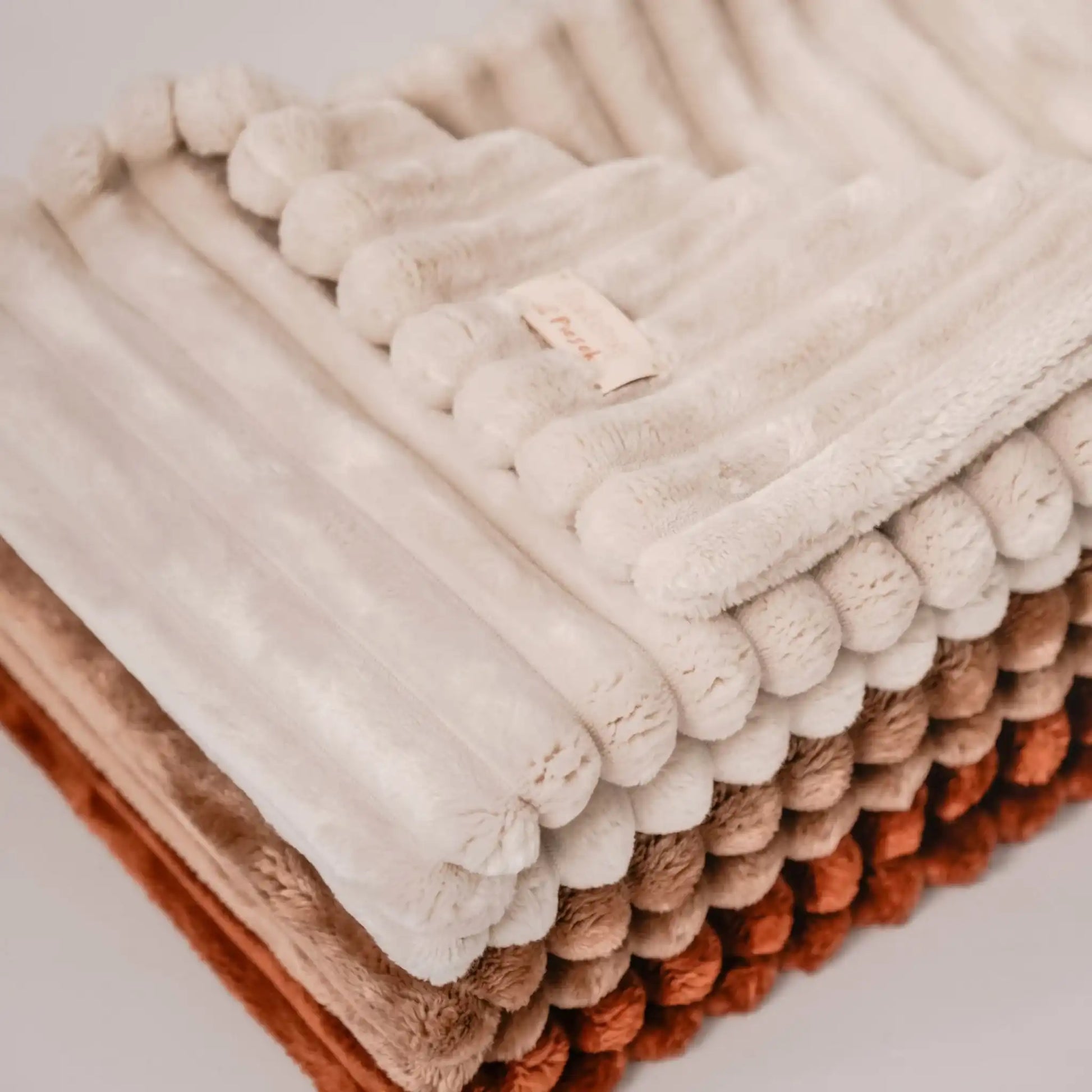 Zbliżenie na detale, ujęcie z góry. 3 kocyki dla psa, w kolorze cynamonek (rudo-brązowy), ciasteczko (brązowy), beza (kremowy), ułożone jeden na drugim od najjaśniejszego do najciemniejszego.