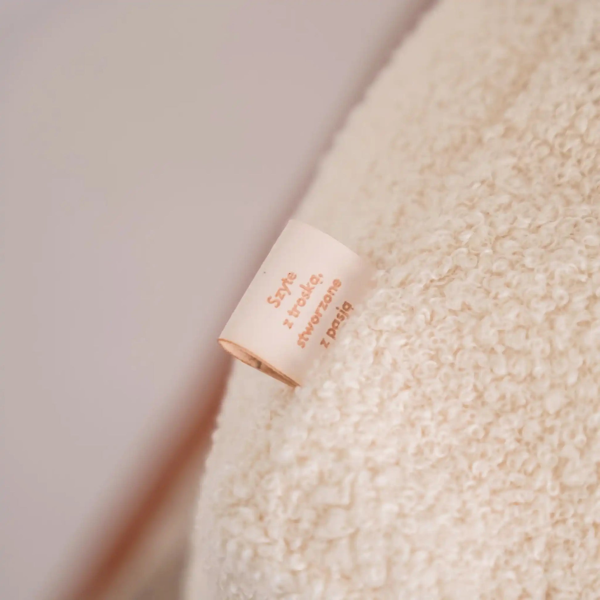 Miękki kosz na zabawki dla psa. Usztywniony pianką tapicerską. Uszyty z tkaniny boucle w kolorze chałwa (kremowy) - ujęcie metki z napisem: szyte z troską, stworzone z pasją.