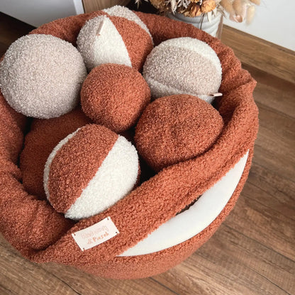 kosz na zabawki dla psa, tkanina boucle, kolor nugat (terakota), kosz znajduje się w jasnym wnętrzu, wypełniony jest piłeczkami z tej samej tkaniny w różnych kolorach, pokazanie detalu tj. zdejmowanego pokrowca