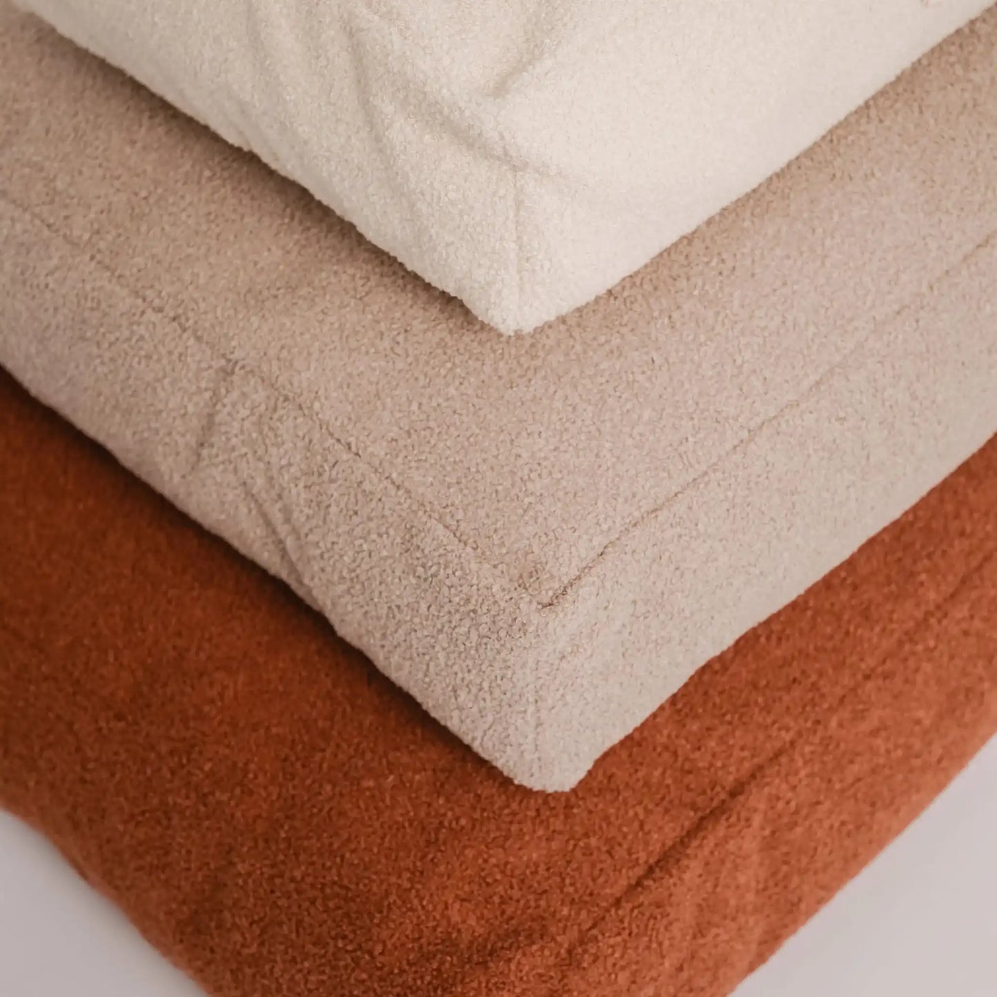 Zbliżenie na trzy materace dla psa (legowiska dla psa), w trzech rozmiarach, od największego do najmniejszego, w kolorze nugat (rudy brąz), pralinka (jasny brąz), chałwa (kremowy), które znajdują się na jasnym czystym tle. Nowoczesna, wysokiej jakości tkanina boucle z certyfikatami bezpieczeństwa.