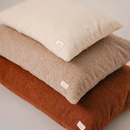 Zbliżenie na trzy poduszki dla psa (legowiska dla psa), w trzech rozmiarach, od największego do najmniejszego, w kolorze nugat (rudy brąz), pralinka (jasny brąz), chałwa (kremowy), które znajdują się na jasnym czystym tle. Nowoczesna, wysokiej jakości tkanina boucle z certyfikatami bezpieczeństwa.