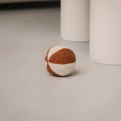 Piłka dla psa z tkaniny boucle. Kolory: rudo brązowy oraz jasny kremowy, piłka znajduje sie w salonie obok stołu, bliski detal.