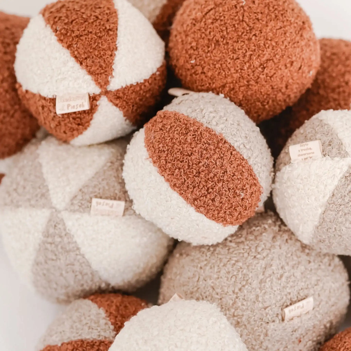 Stos wielu piłeczek różnokolorowych (rudo-brązowy, jasny brąz, kremowy), zbliżenie, metki. Tkanina boucle. Piłka dla psa.